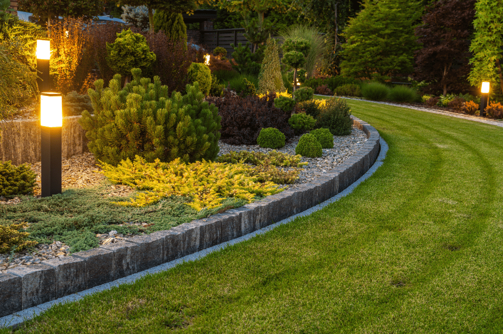 A well-maintained landscape design featuring a stone wall illuminated by decorative lights, designed in Eagle, Idaho.